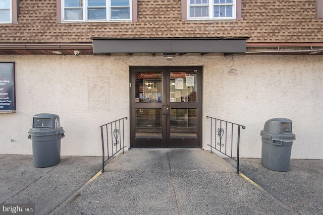 property entrance with a shingled roof, stucco siding, and french doors