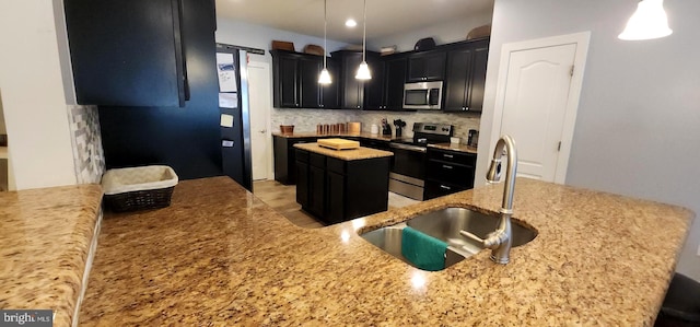 kitchen with a kitchen island, appliances with stainless steel finishes, decorative light fixtures, light stone countertops, and sink