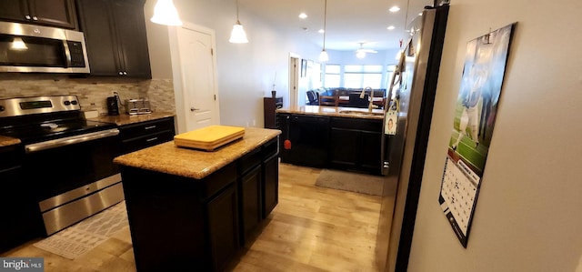 kitchen featuring a kitchen island, appliances with stainless steel finishes, pendant lighting, decorative backsplash, and light hardwood / wood-style floors