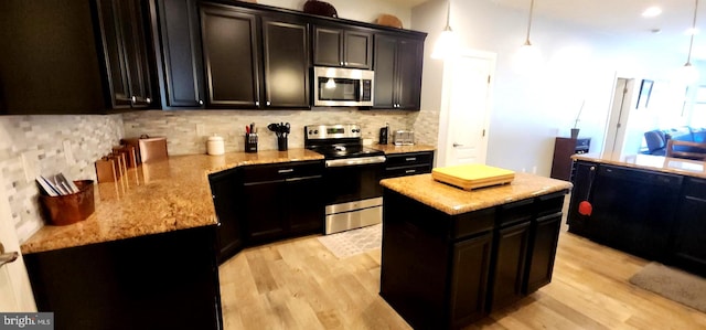 kitchen with a kitchen island, pendant lighting, appliances with stainless steel finishes, and light hardwood / wood-style flooring