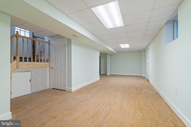 basement featuring a paneled ceiling and light hardwood / wood-style floors