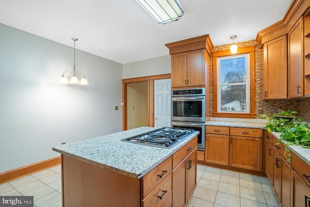 kitchen with an inviting chandelier, hanging light fixtures, appliances with stainless steel finishes, a kitchen island, and light stone counters