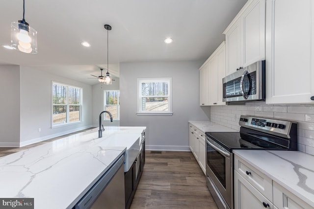 kitchen featuring dark hardwood / wood-style flooring, light stone counters, white cabinets, appliances with stainless steel finishes, and decorative light fixtures