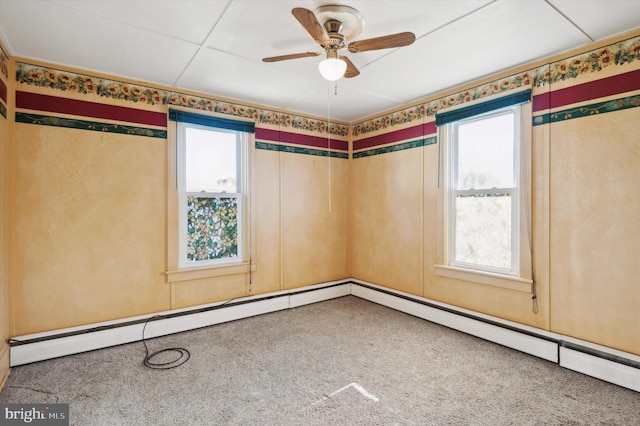 carpeted spare room featuring a drop ceiling, ceiling fan, and a wealth of natural light