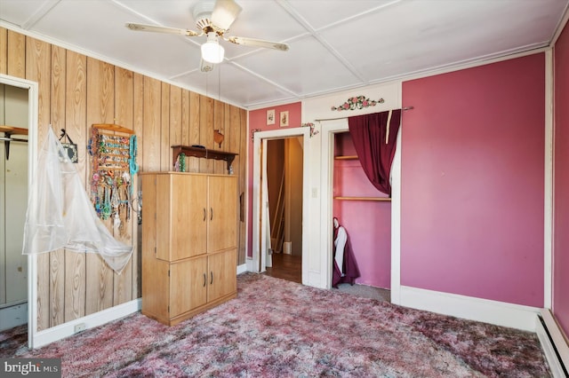 carpeted bedroom with wood walls, a baseboard heating unit, crown molding, and ceiling fan