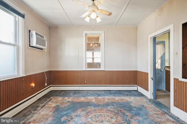 empty room with baseboard heating, wooden walls, ceiling fan, and plenty of natural light