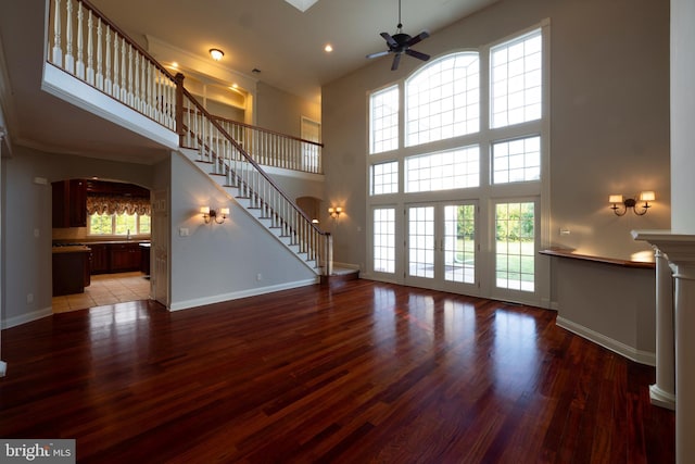 unfurnished living room featuring ceiling fan, a high ceiling, wood-type flooring, and a healthy amount of sunlight