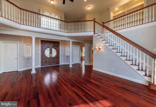 foyer entrance with dark wood-type flooring, ornate columns, and a towering ceiling