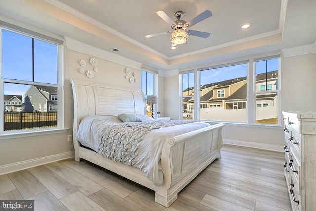 bedroom featuring light hardwood / wood-style floors, a raised ceiling, multiple windows, and ceiling fan