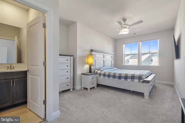 bedroom with ensuite bath, light carpet, ceiling fan, and sink