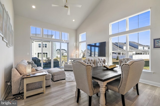 dining space with light hardwood / wood-style flooring, ceiling fan, and a towering ceiling