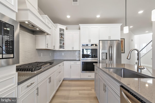 kitchen featuring dark stone counters, sink, custom range hood, appliances with stainless steel finishes, and decorative light fixtures