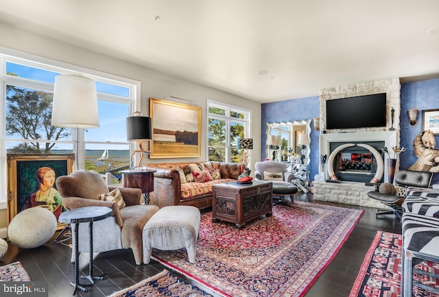 living room with a stone fireplace and dark wood-type flooring