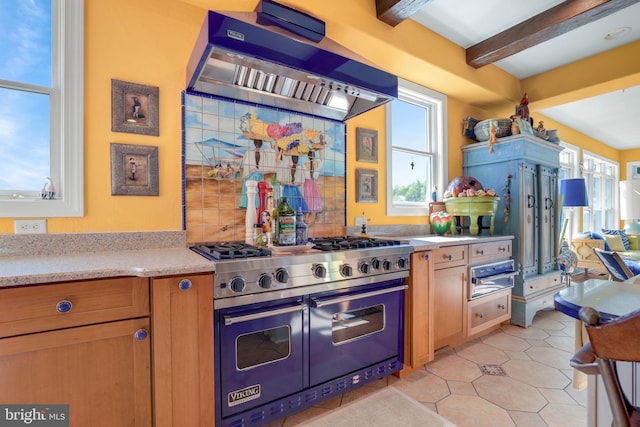 kitchen featuring beam ceiling, a wealth of natural light, range with two ovens, and wall chimney range hood