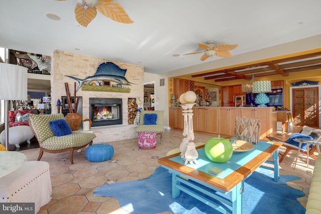 tiled living room featuring beamed ceiling, ceiling fan, a stone fireplace, and sink