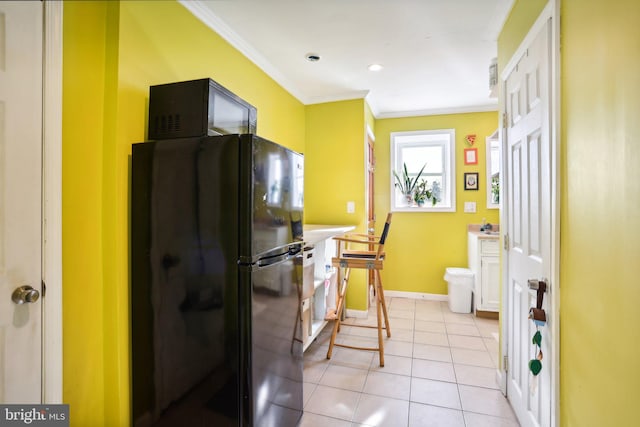 kitchen featuring white cabinets, black fridge, crown molding, and light tile patterned flooring