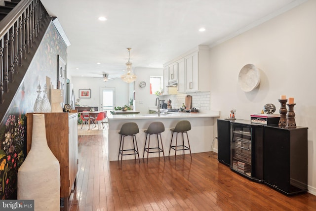 kitchen featuring kitchen peninsula, a kitchen breakfast bar, tasteful backsplash, hardwood / wood-style flooring, and white cabinets