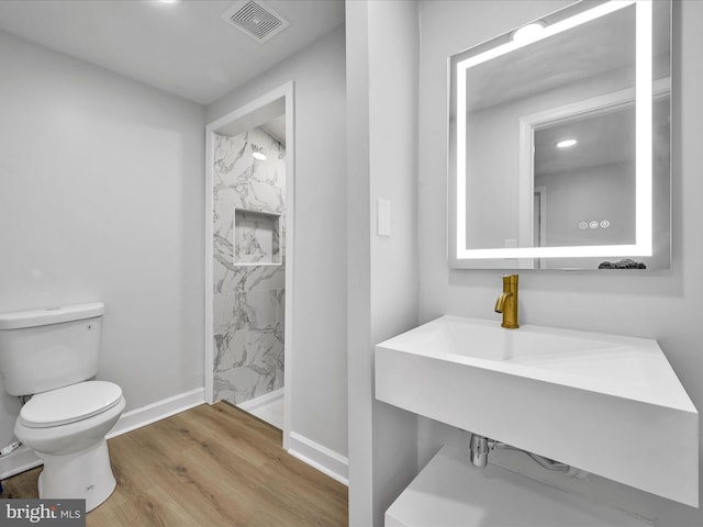 bathroom featuring tiled shower, wood-type flooring, sink, and toilet