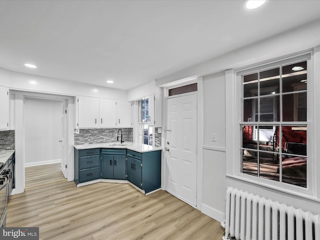 kitchen with radiator heating unit, decorative backsplash, sink, white cabinetry, and light hardwood / wood-style flooring