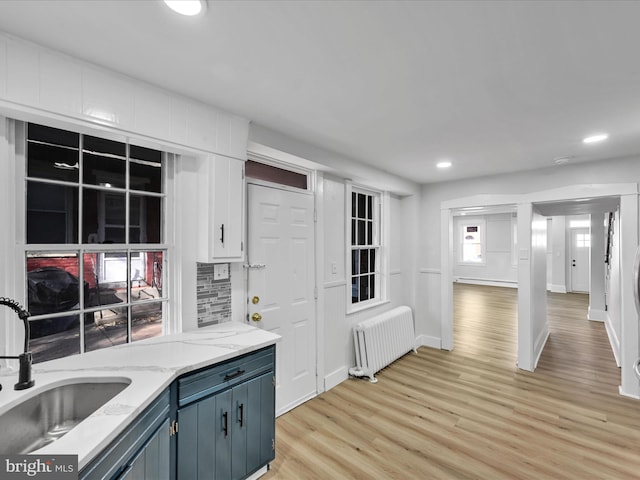 kitchen with light hardwood / wood-style floors, light stone counters, radiator, sink, and blue cabinetry