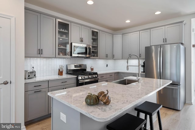 kitchen featuring sink, stainless steel appliances, light stone countertops, and a center island with sink