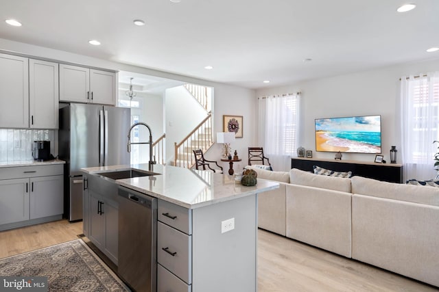 kitchen with light wood-type flooring, stainless steel appliances, a kitchen island with sink, and gray cabinetry