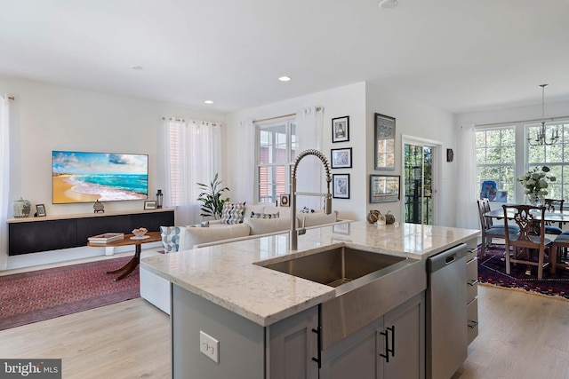 kitchen with sink, dishwasher, a kitchen island with sink, light stone counters, and decorative light fixtures