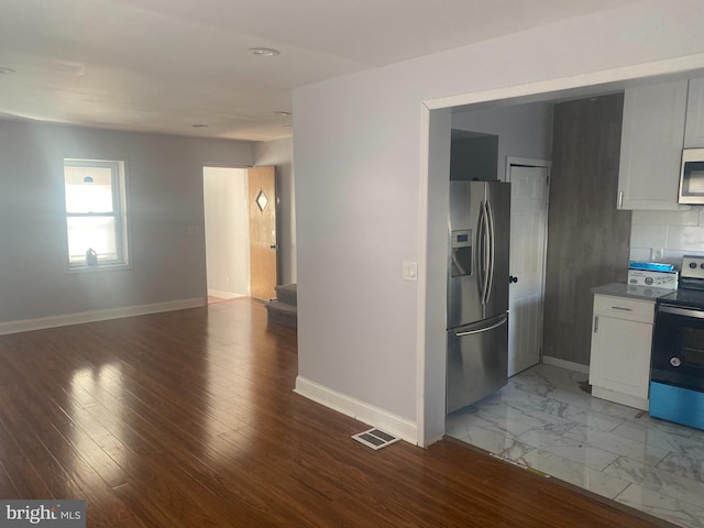 kitchen with decorative backsplash, white cabinetry, hardwood / wood-style flooring, and stainless steel appliances