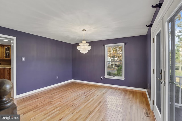 spare room with a wealth of natural light, a notable chandelier, and light hardwood / wood-style flooring