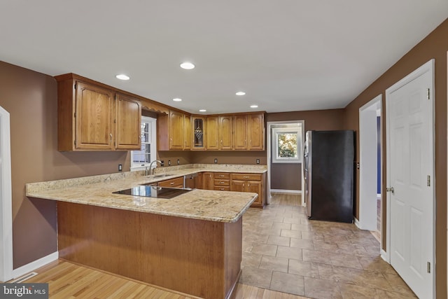 kitchen with light hardwood / wood-style floors, black electric stovetop, kitchen peninsula, sink, and stainless steel refrigerator