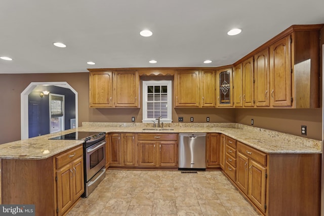 kitchen with kitchen peninsula, appliances with stainless steel finishes, sink, and light stone counters