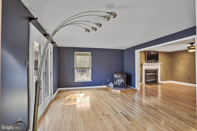 unfurnished living room with a wood stove, ceiling fan, and light hardwood / wood-style flooring