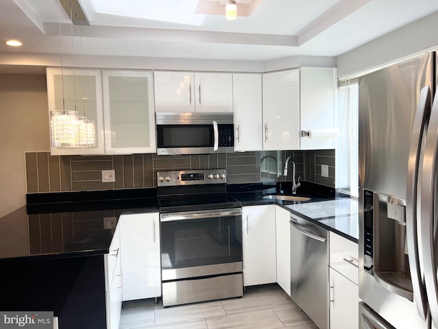 kitchen featuring white cabinets, backsplash, appliances with stainless steel finishes, a tray ceiling, and sink