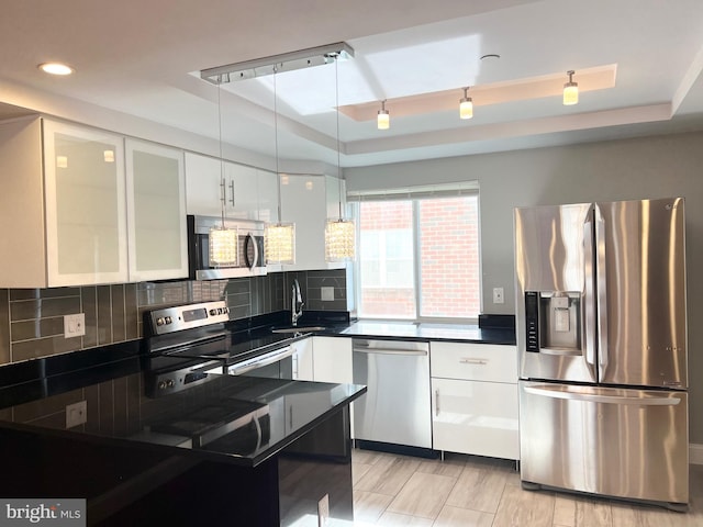 kitchen with decorative backsplash, appliances with stainless steel finishes, a tray ceiling, and white cabinetry