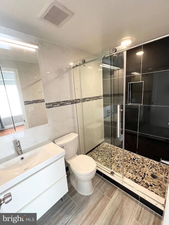 bathroom featuring tile walls, vanity, a shower with shower door, and toilet