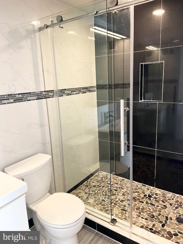 bathroom featuring tile walls, vanity, a shower with shower door, and toilet