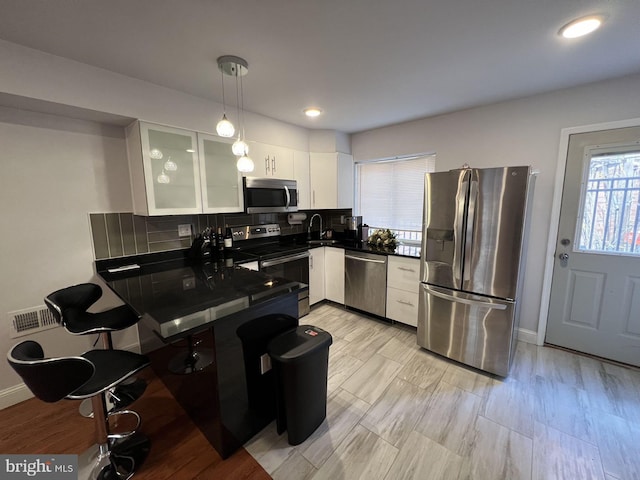 kitchen with stainless steel appliances, a breakfast bar, pendant lighting, white cabinetry, and tasteful backsplash