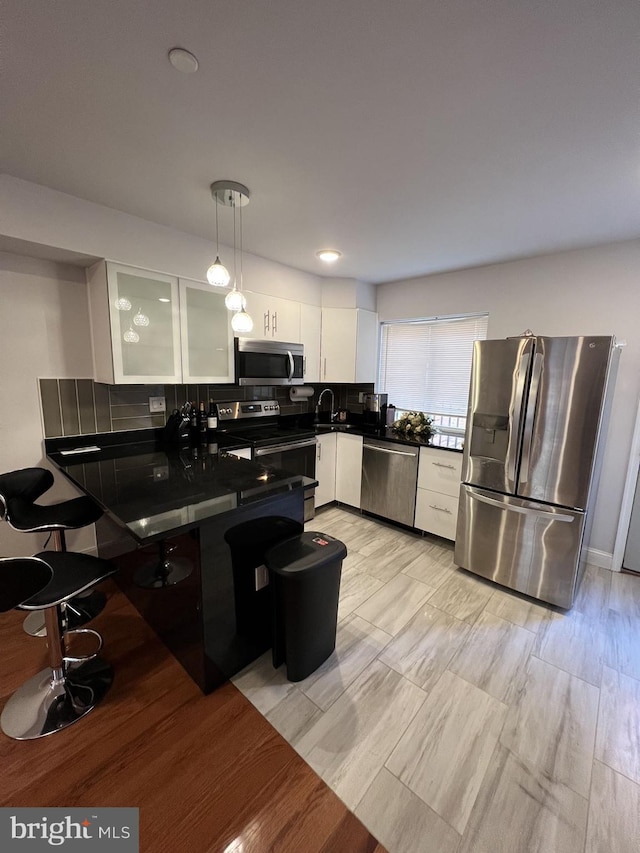 kitchen with tasteful backsplash, white cabinetry, sink, pendant lighting, and stainless steel appliances