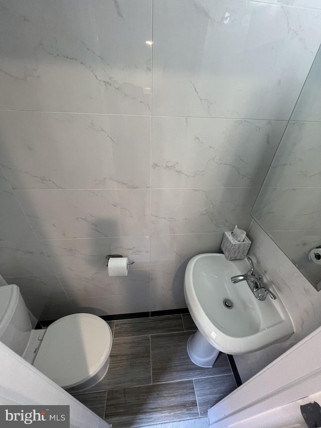 bathroom with toilet, sink, and tile walls