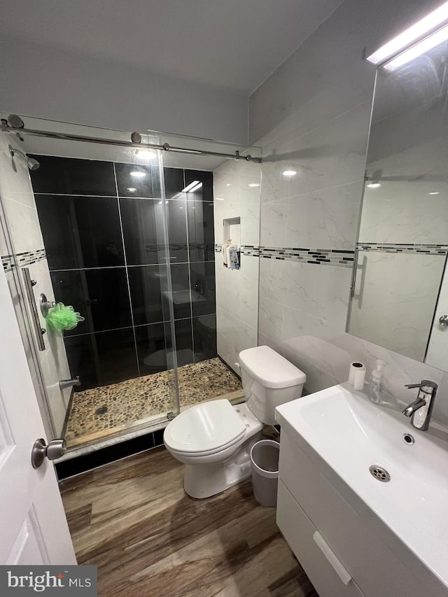 bathroom with a shower with door, toilet, hardwood / wood-style floors, tile walls, and vanity