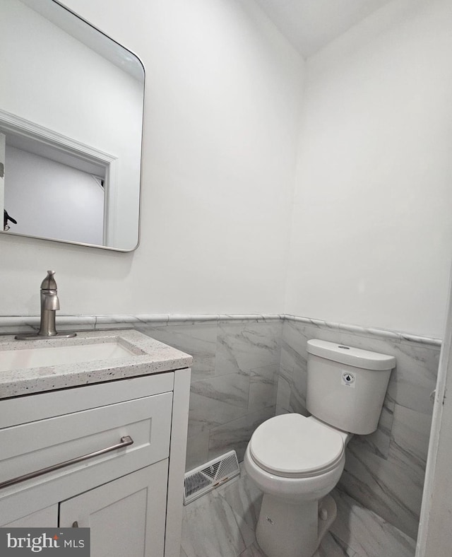 bathroom with toilet, vanity, and tile walls