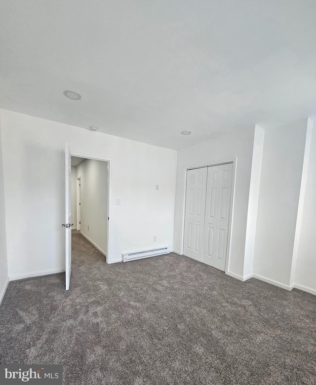 unfurnished bedroom featuring a baseboard heating unit, dark colored carpet, and a closet