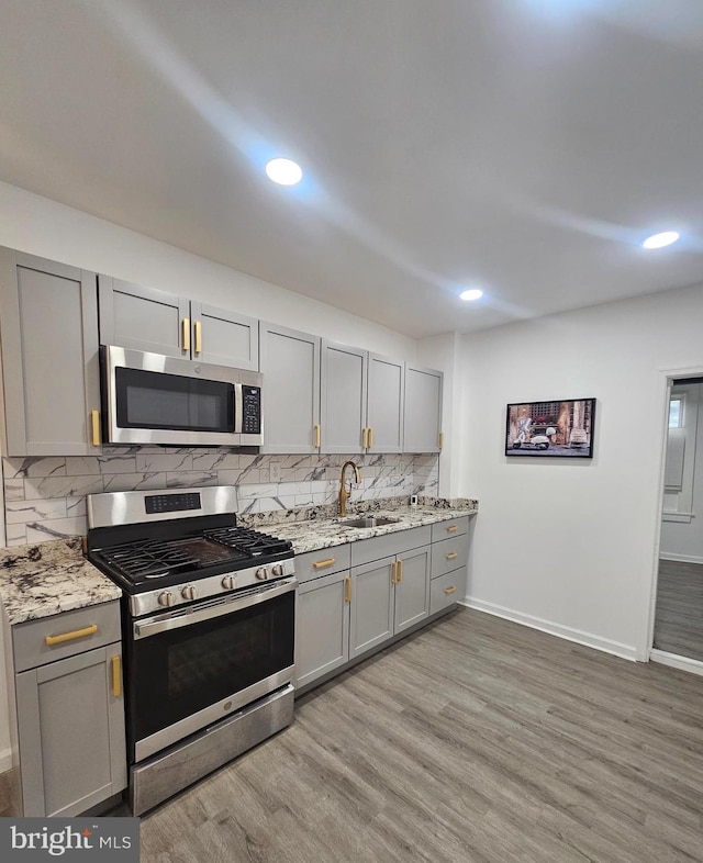 kitchen featuring gray cabinets, appliances with stainless steel finishes, light hardwood / wood-style floors, and light stone countertops