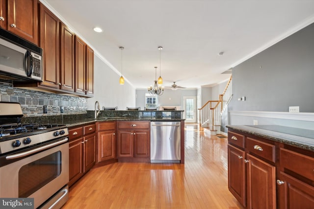 kitchen featuring hanging light fixtures, dark stone countertops, ornamental molding, appliances with stainless steel finishes, and light hardwood / wood-style floors