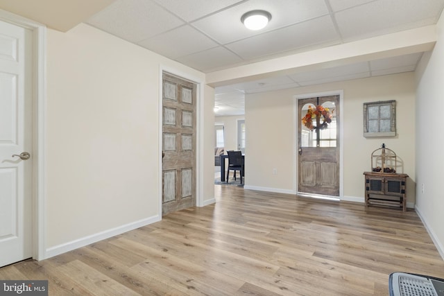 foyer entrance with a drop ceiling, light wood finished floors, and baseboards