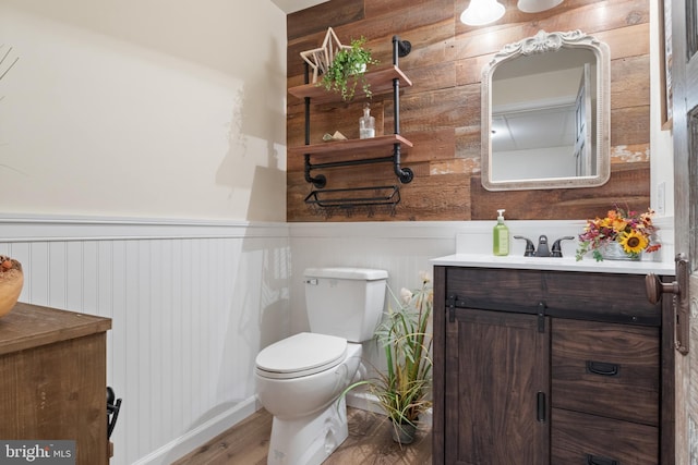 half bathroom with wood finished floors, a wainscoted wall, toilet, and vanity