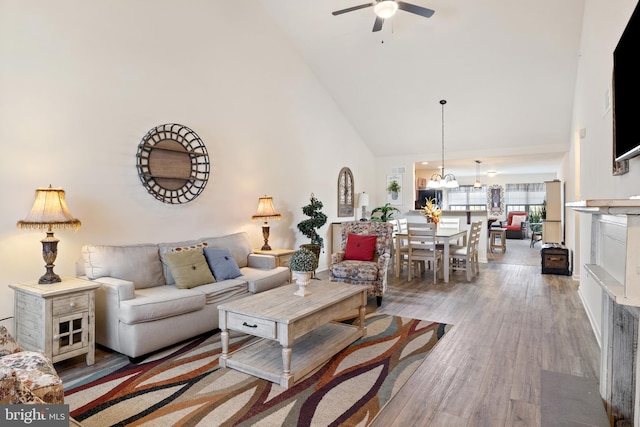 living area featuring high vaulted ceiling, a ceiling fan, a chandelier, and wood finished floors