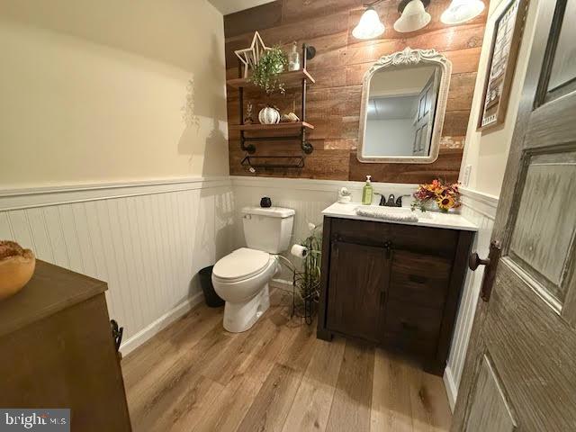 bathroom featuring toilet, wood walls, vanity, and hardwood / wood-style floors