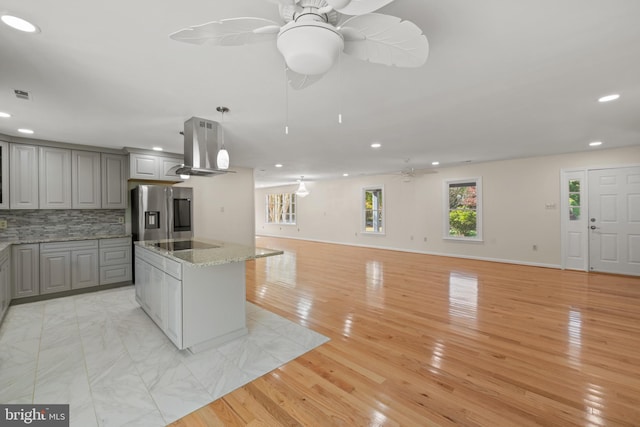 kitchen featuring stainless steel fridge with ice dispenser, backsplash, island exhaust hood, stone countertops, and gray cabinets