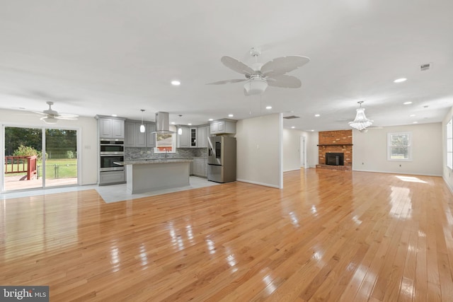 unfurnished living room featuring ceiling fan, light hardwood / wood-style floors, and a brick fireplace